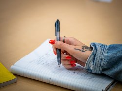 A close up photo of hand with red fingernails holding a pen while taking notes.