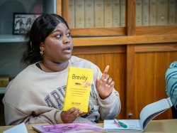 A student gestures, as she asks a question while holding a book titled Brevity.