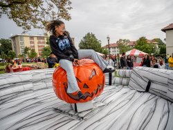 A young woman rides a mechanical pumpkin.