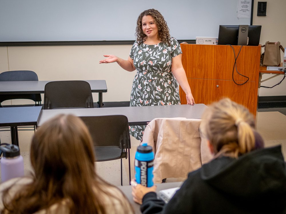 A woman stands in front of students, gesturing.