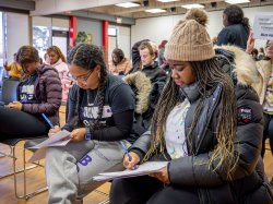 Students, one wearing a winter cap and coat, fill out forms.