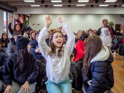 A room full of students with one in the center front row with her hands in the air.