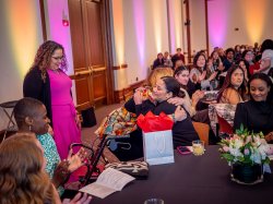 A professor hugs a student seated at a table after presenting her with an award.