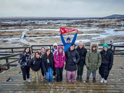 A group of students and professors stand with a Montclair State University pennant in front of a snowy landscape.