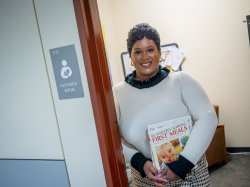 A student stands holding books in a lactation room doorway.