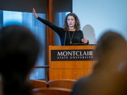 A professor gestures while speaking at a lectern.