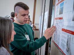 A student discusses his research poster with a faculty member.
