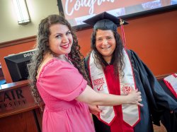 A young woman adjusts her mother's graduation stole.