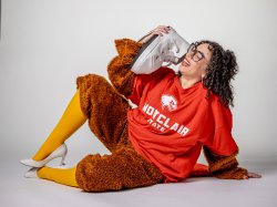 A costumed Eliza Andrus holds a sneaker as a phone while laughing.