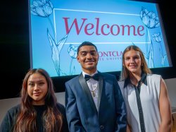 Three students in front of a welcome sign