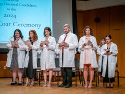 Students wearing white lab coats read an oath onstage.