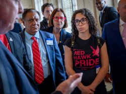 A woman wearing a Red Haw Pride t-shirt listens to a state senator.