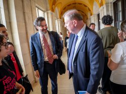 Two men smile in a hallway.
