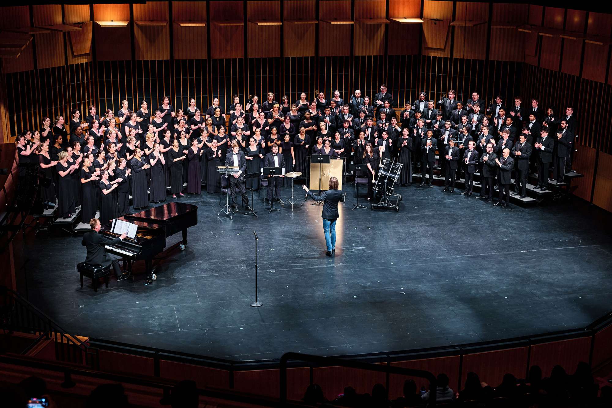 A chorus on stage with a man conducting.