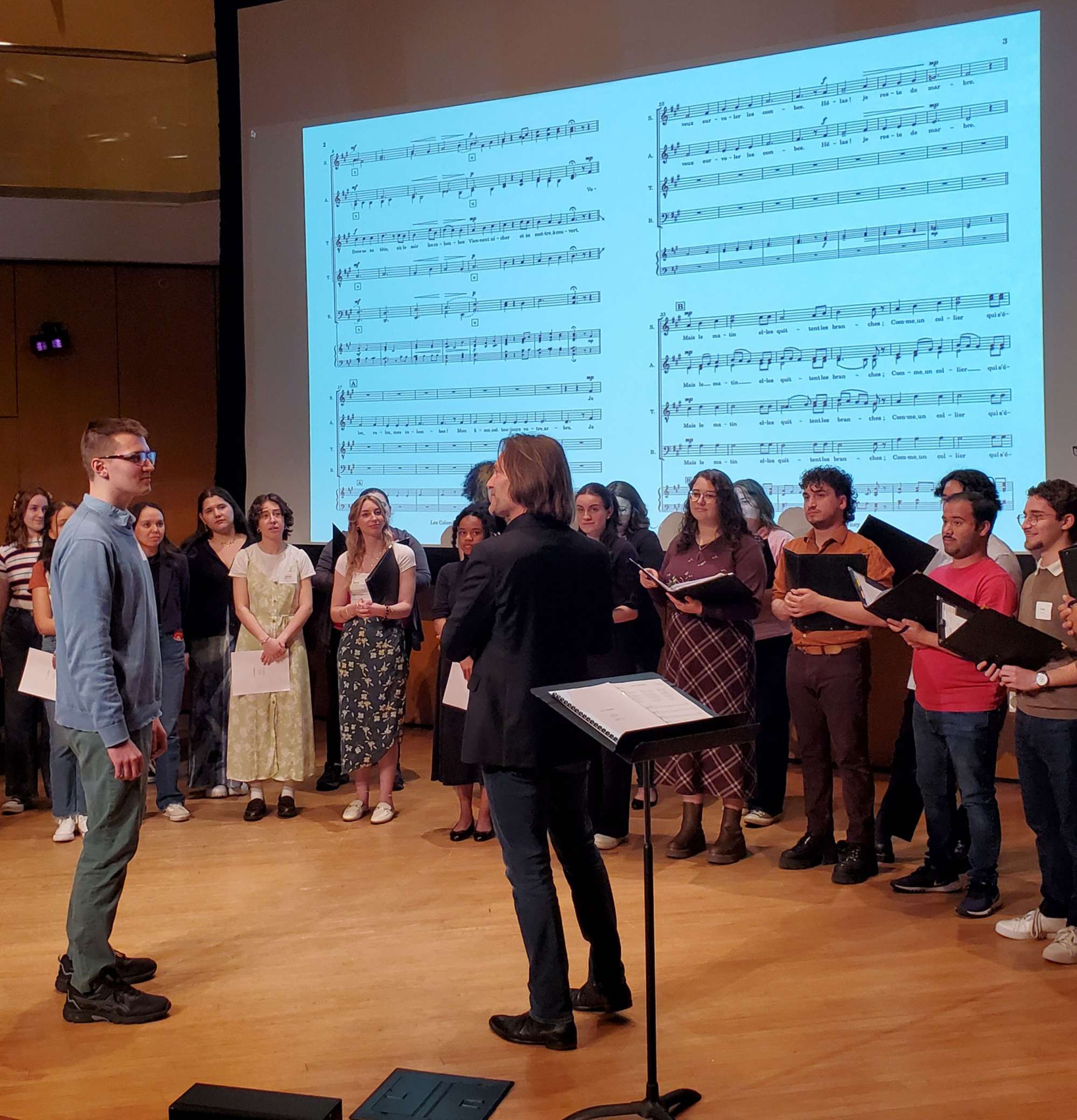 Singers stand in front of a projection of sheet music.