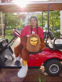 Aylin Alvarez-Santiago holds Ricky’s mascot head while seated in a red golf cart.