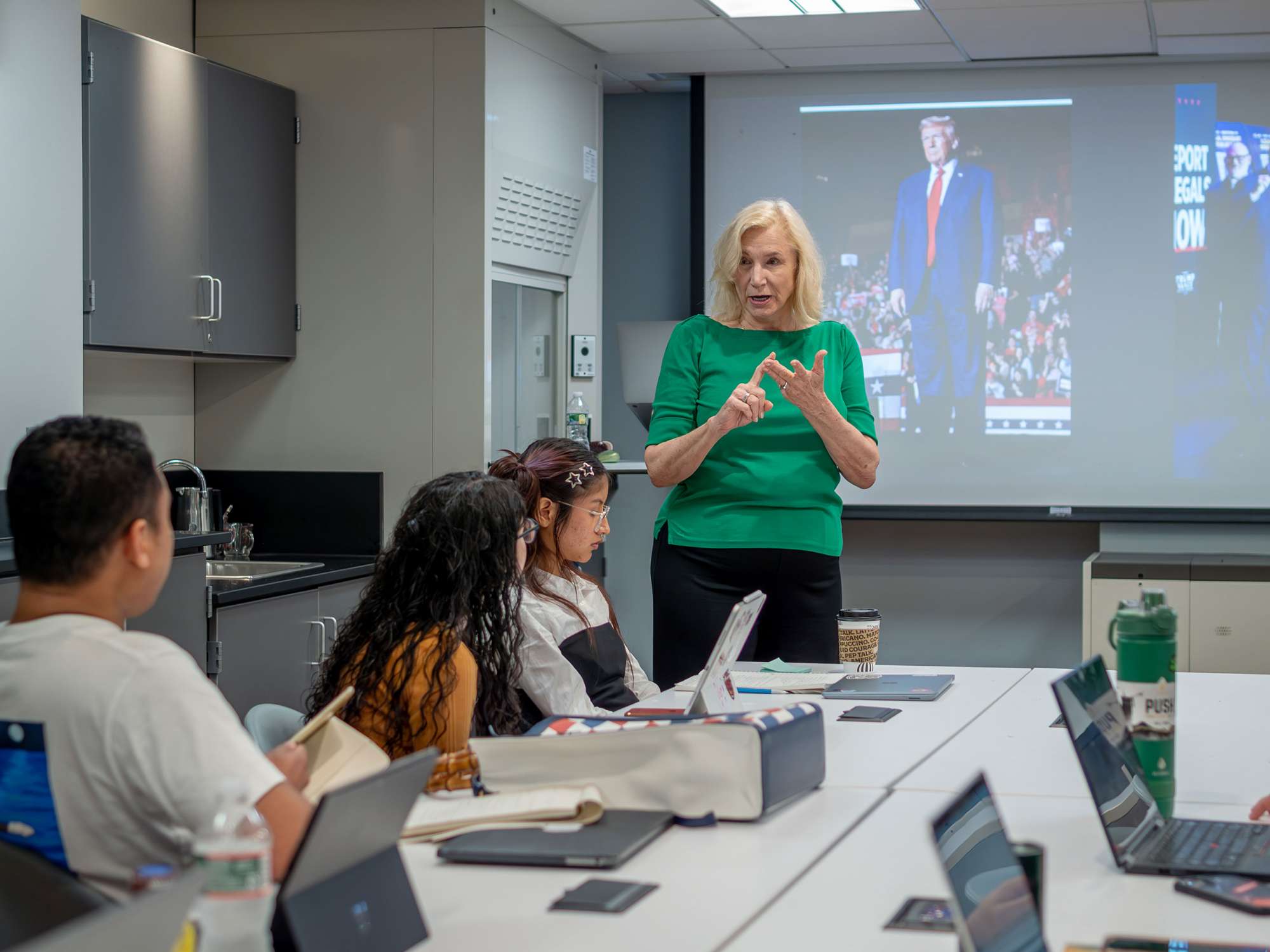 A professor gestures from the front of a filled classroom.