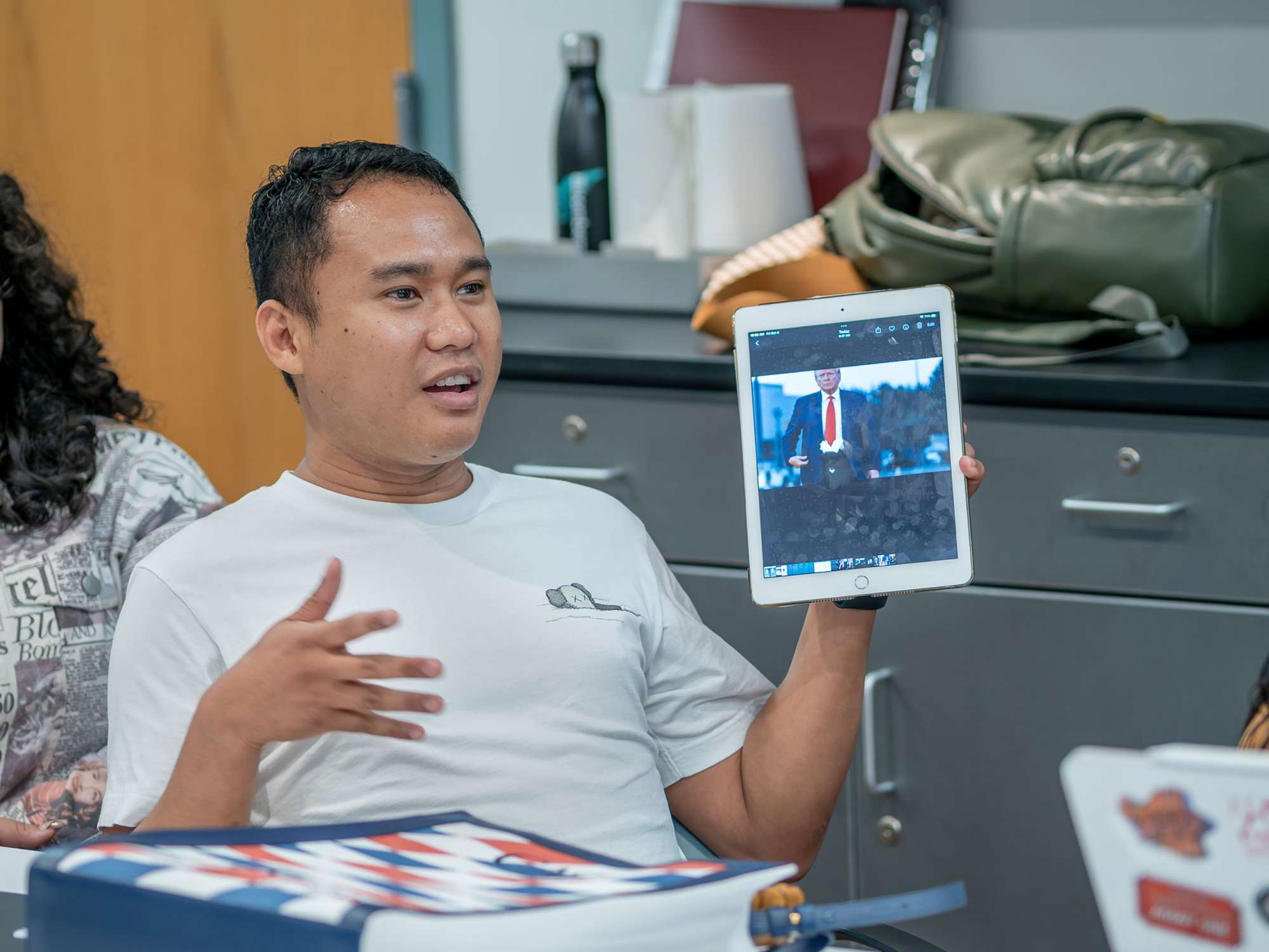 Student Nelson Dela Cruz holds a tablet with a manipulated image of Donald Trump in a shorter tie.