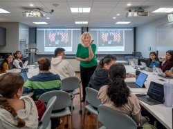 A professor gestures from the front of a filled classroom.