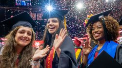 Three graduates in caps and gowns smiling with confetti falling around them