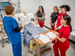 Nursing students gathered around medical manikin in simulation lab.