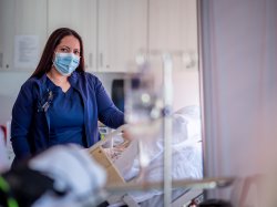 Online MSN student standing over medical manikin in the Simulation Center.