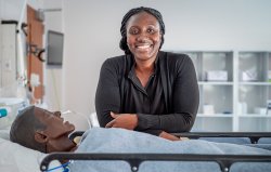 Elsie Alabi-Gonzalez, Clinical Specialist, standing in the School of Nursing's Simulation Center in front of a medical manikin.