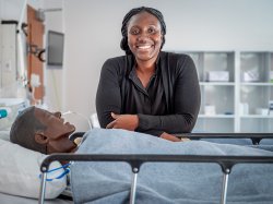 Elsie Alabi-Gonzalez, Clinical Specialist, standing in the School of Nursing's Simulation Center in front of a medical manikin.