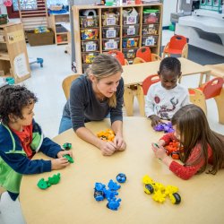 Photo of teacher with young children and blocks in classroom.
