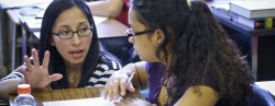 Photo of female professor speaking with student in class.