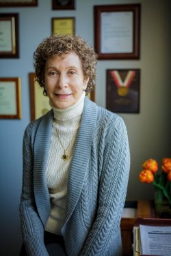 photo of Professor Marilyn Tayler standing in her office. A wall of framed certificates and awards is behind her