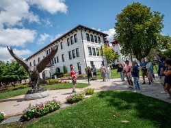 A man standing in front of a giant red hawk statue speaks to a group of people about Montclair State University.