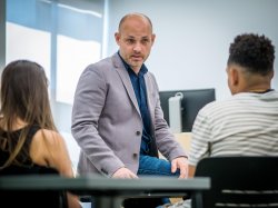 professor leaning on desk speaking to students