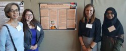 Photo of a professor and three students standing next to a research poster.