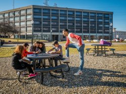 Students sitting around a table with Blanton Hall in the background and blue skies