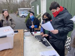 Students stand outside, masked, sorting and scanning documents