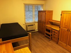 A bedroom in a Hawk Crossing's apartment featuring an AC, desk, bed and closet space.