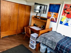 One side of the room of a Double in Stone Hall with a desk and television.