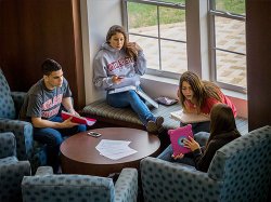 Students sitting around in a Residence Hall showing one-another things on an iPad and studying.