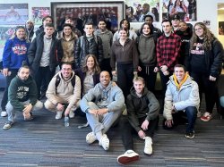 Students in two rows, some sitting and others standing, smiling and looking relaxed.
