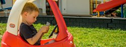 Image of a child sitting in a play car dialing on a play phone.