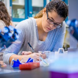 Student in laboratory taking notes around equipment