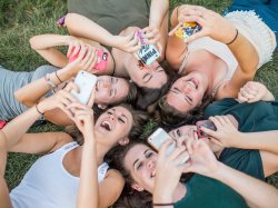 Female Montclair State University students laying in a circle while taking selfies with cellphones.