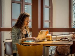 Photo of student working on laptop at table in campus building.