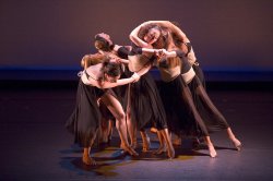 Photo of dancers in tight group, arms interlocked.