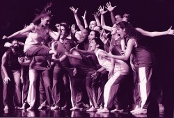 Photo of large troupe of dancers crowded close on stage.