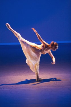 Photo of single dancer in leg-lift pose in spotlight.