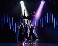 Group of dancers tossing another dancer into the air under spotlights