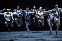 seven dancers wearing business suits dancing on stage facing viewer