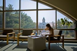 Student studying in library in front of large window overlooking College Hall.